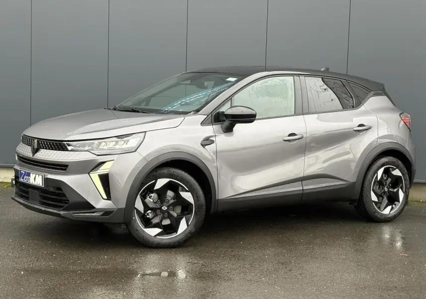 Renault Captur 2025 gris Cassiopée avec toit noir, vue 3/4 avant droit sur sol humide, jantes noires distinctives.