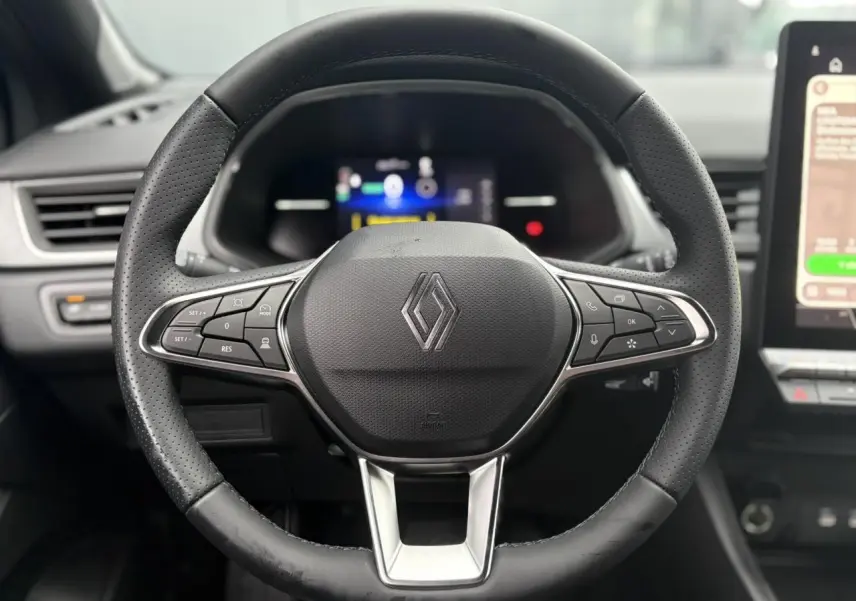 Vue rapprochée du volant en cuir noir perforé du Renault Captur 2025 avec commandes intégrées et tableau de bord numérique flou.