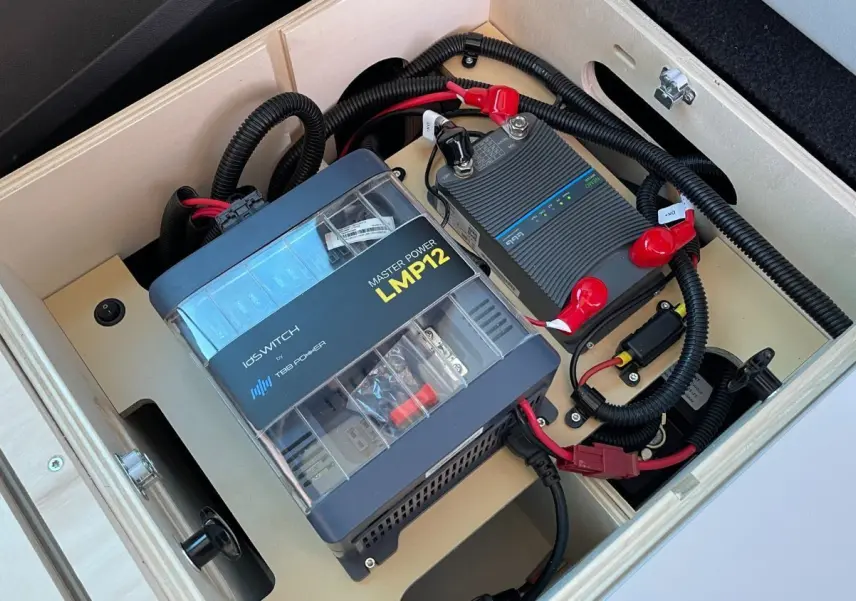 Vue rapprochée de la batterie auxiliaire AGM et du convertisseur électrique dans le coffre du Renault Trafic Fourgon gris comète.