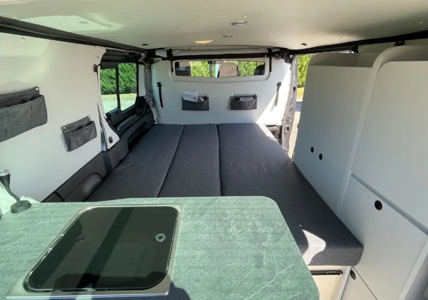 Intérieur du Renault Trafic Fourgon gris Comète, vue arrière montrant le lit double et les rangements blancs intégrés.