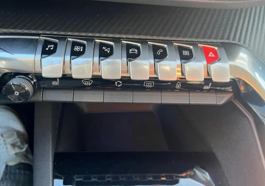 Gros plan sur la rangée de boutons argentés et rouge du tableau de bord du Peugeot 3008 2023, intérieur noir.