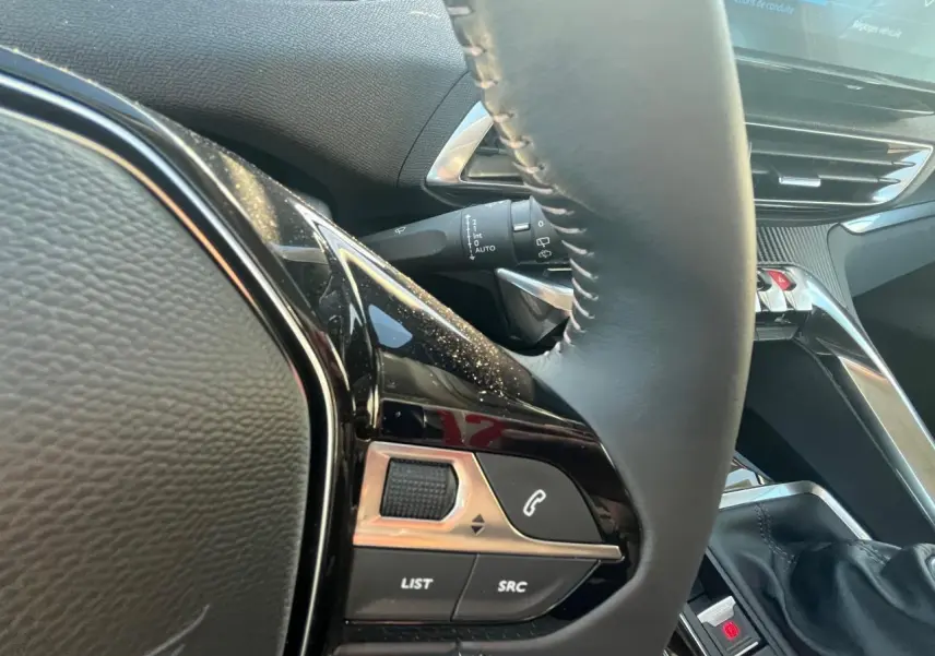 Gros plan sur le volant côté gauche du Peugeot 3008 gris Artense, avec commandes audio et écran tactile visible en arrière-plan.