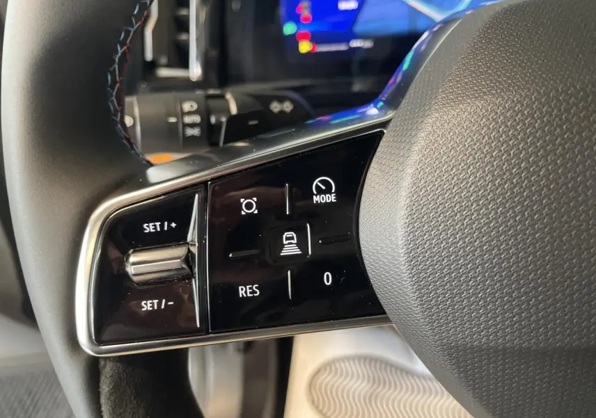 Gros plan sur les commandes gauche du volant textile Alcantara du Renault Austral gris satin mat, avec affichage numérique en arrière-plan.