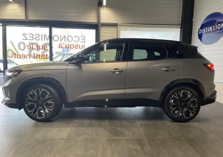 Profil côté gauche du Renault Austral gris satin mat avec toit noir et jantes alliage 20 pouces en intérieur showroom.