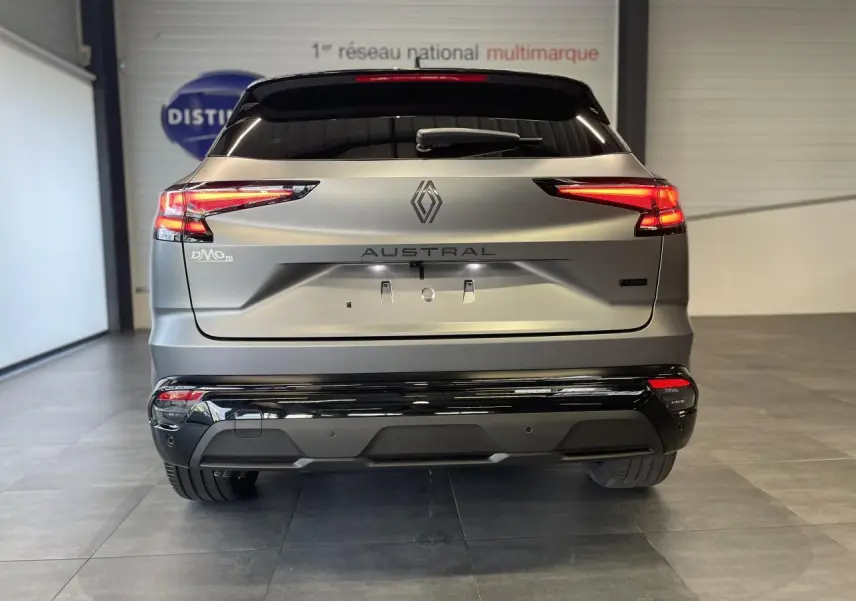 Vue arrière du Renault Austral 2025 gris satin mat avec toit noir et feux LED allumés en intérieur showroom.