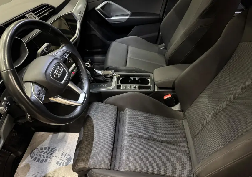 Vue intérieure côté conducteur de l'Audi Q3 Business 2019 avec sellerie tissu gris et volant multifonction.