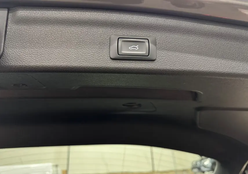 Bouton d'ouverture électrique du coffre sur la garniture intérieure noire d'un Audi Q3 Business gris.