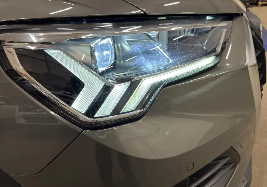 Gros plan sur le phare avant droit LED dynamique d’un Audi Q3 Business gris, soulignant ses lignes modernes et précises.