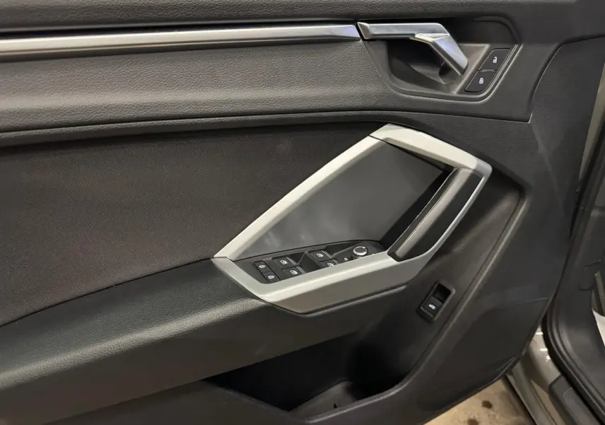 Gros plan sur la porte avant gauche de l'Audi Q3 Business gris, avec commandes de vitres et inserts noir brillant.