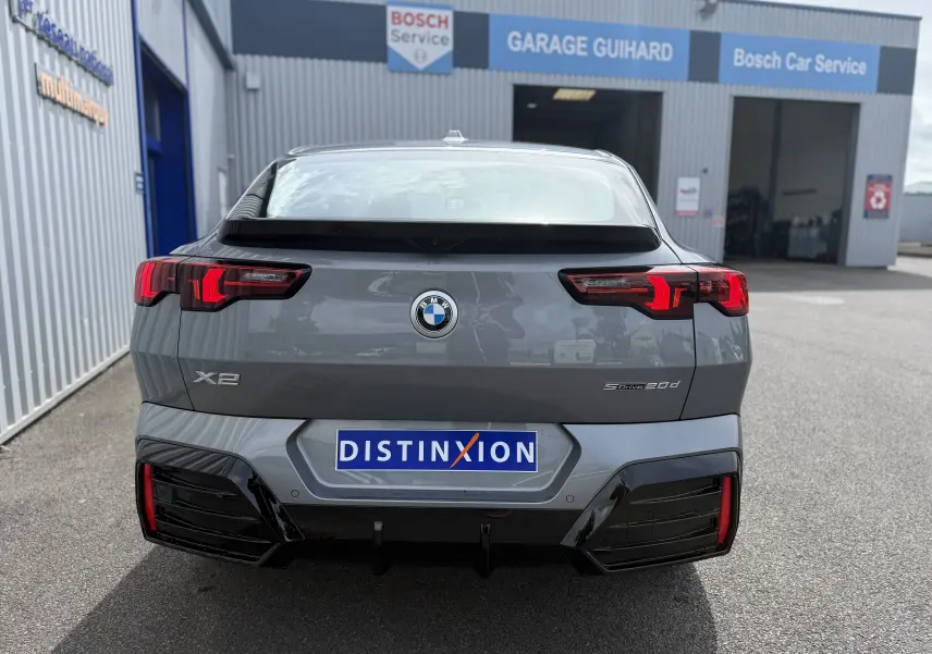 Vue arrière d'une BMW X2 Skyscraper gris métallisé avec feux LED distinctifs, stationnée devant un garage Bosch.