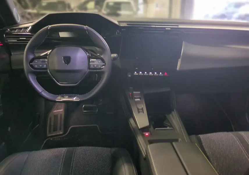 Intérieur noir de la Peugeot 308 2025, vue frontale du poste de conduite avec volant cuir et écran tactile central.