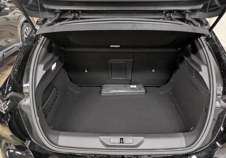 Coffre ouvert vu de l'arrière d'une Peugeot 308 noir Perla, avec un espace de chargement propre et un kit de sécurité posé.