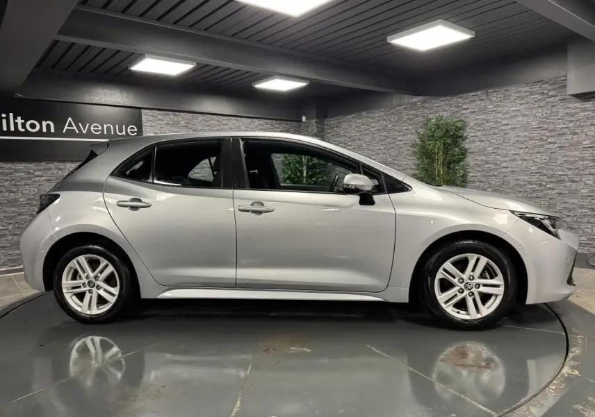 Profil côté gauche d'une Toyota Corolla hybride gris métallisé avec jantes alliage 16 pouces dans un showroom.