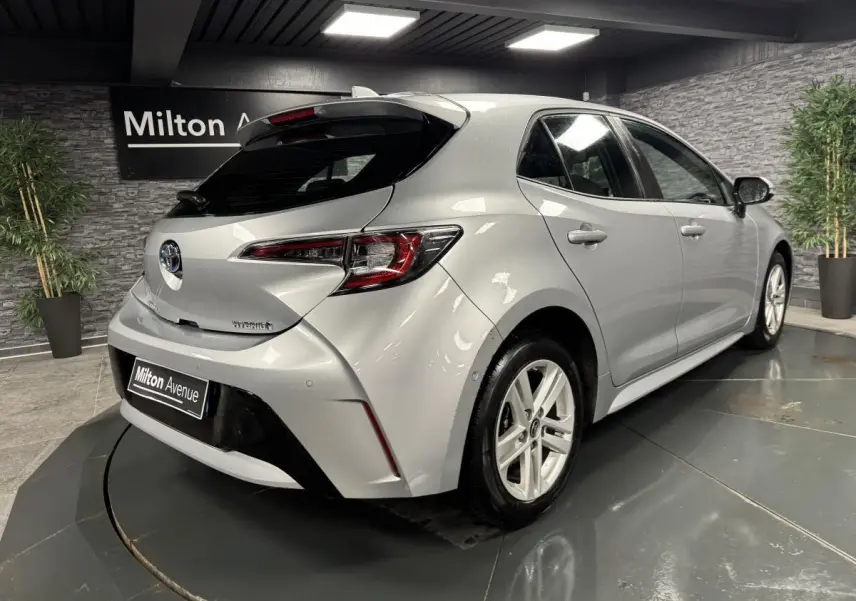 Toyota Corolla hybride gris vue 3/4 arrière droit en intérieur avec jantes alliage et antenne aileron de requin