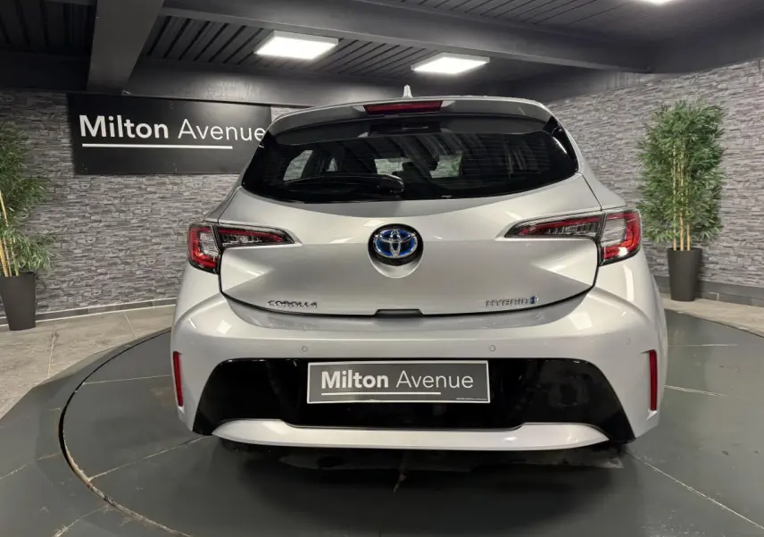 Vue arrière d'une Toyota Corolla hybride gris métallisé avec logo Toyota et feux arrière LED dans un showroom.