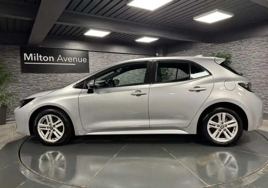 Profil côté gauche d'une Toyota Corolla hybride gris métallisé, avec jantes alliage et poignées couleur carrosserie.