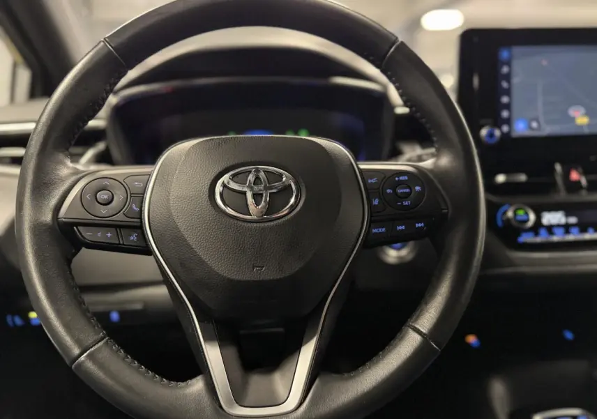Volant cuir noir Toyota Corolla Hybride 2022 vu de face, avec commandes multifonctions et écran tactile en arrière-plan.
