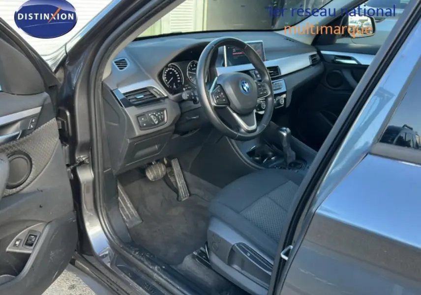 Intérieur côté conducteur d’un BMW X1 gris foncé 2022, volant sport et tableau de bord visible en lumière naturelle.