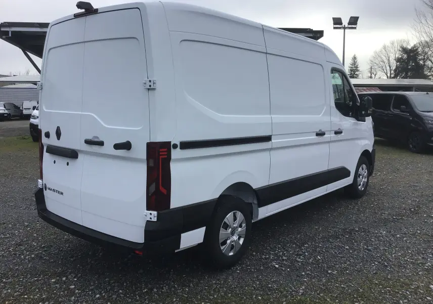 Vue 3/4 arrière droite d’un Renault Master blanc, fourgon utilitaire avec feux arrière verticaux et protections noires sur les flancs.