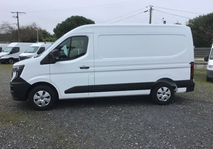 Vue de profil côté gauche d’un utilitaire blanc Renault Master L2H2 avec bandes noires et jantes argentées sur sol gravillonné.
