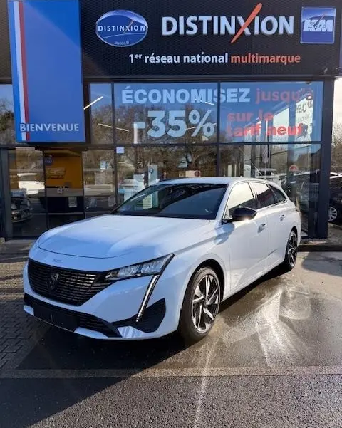 Peugeot 308 Hybrid blanc vue 3/4 avant droit, avec calandre noire et feux LED distinctifs, devant un showroom.