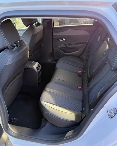 Vue intérieure côté arrière droit de la banquette arrière en tissu et cuir dans une Peugeot 308 Hybrid 145 e-DCS6 Allure blanche.