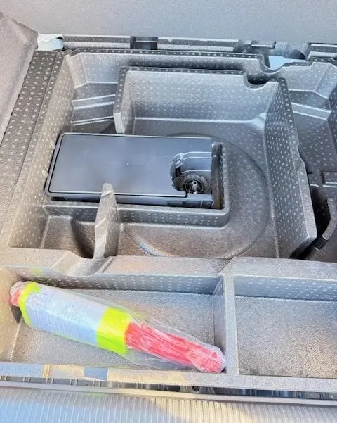 Vue rapprochée du rangement sous le plancher du coffre de la Peugeot 308 Hybrid 145 e-DCS6 Allure blanche, avec équipement de sécurité visible.