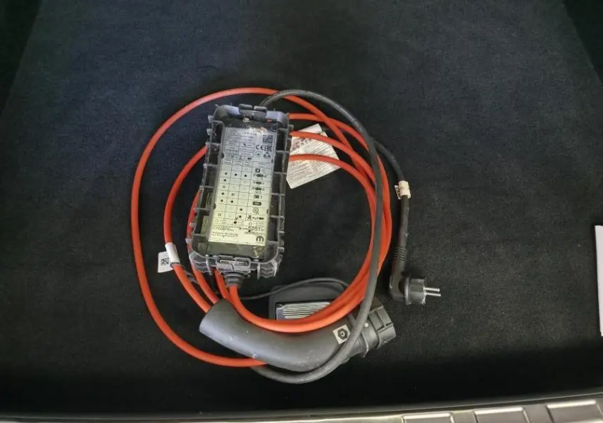 Câble de recharge orange et noir posé dans le coffre d'une Peugeot 408 gris métallisé, vue plongeante.