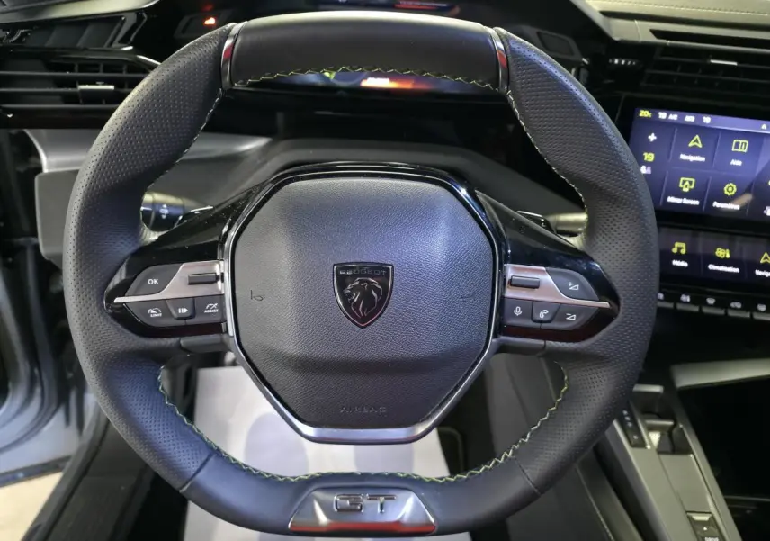 Volant cuir perforé noir avec surpiqûres vertes et badge GT, tableau de bord numérique Peugeot 408 hybride rechargeable.