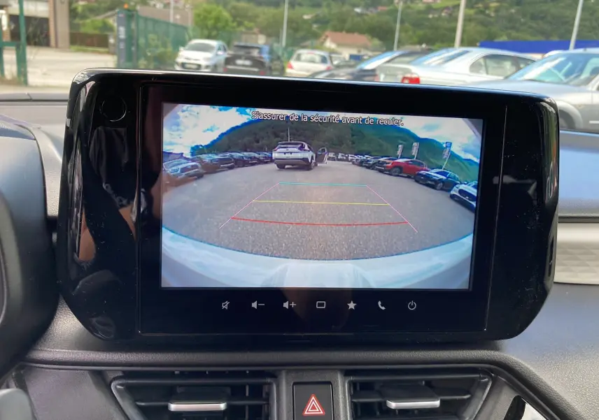 Écran central montrant la caméra de recul d'une Suzuki Swift blanche, vue depuis l'intérieur avant.