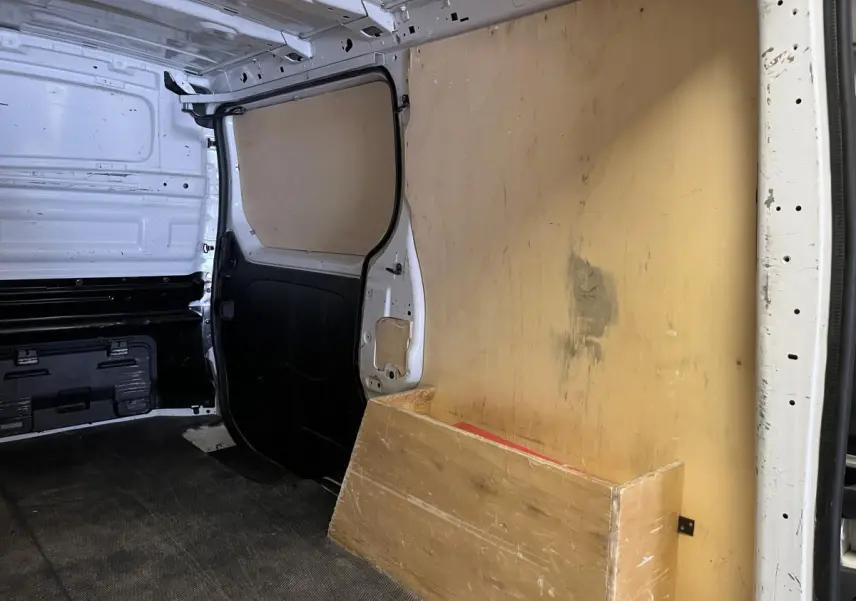 Intérieur du compartiment de chargement du Nissan Primastar blanc avec protection bois et cloison tôlée noire.