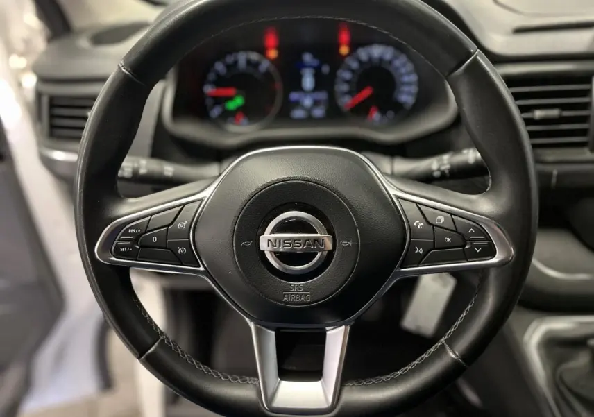 Vue rapprochée du volant en cuir noir du Nissan Primastar 2022 avec commandes intégrées et tableau de bord flou en arrière-plan