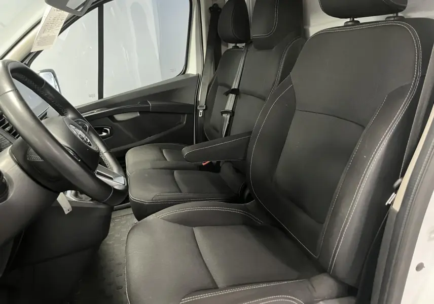 Vue intérieure côté conducteur du Nissan Primastar blanc 2022, sièges tissu gris avec accoudoir et volant simili-cuir.