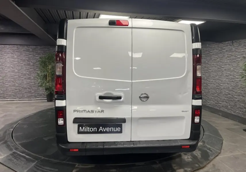 Vue arrière d'un utilitaire Nissan Primastar blanc avec portes battantes et feux verticaux rouges.