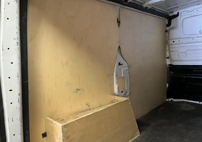 Vue intérieure du compartiment de chargement d'un utilitaire Nissan Primastar blanc avec plancher et protections latérales en bois.