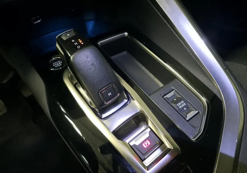 Gros plan sur la console centrale noire du Peugeot 5008 gris, avec levier de boîte auto et bouton Drive Mode.