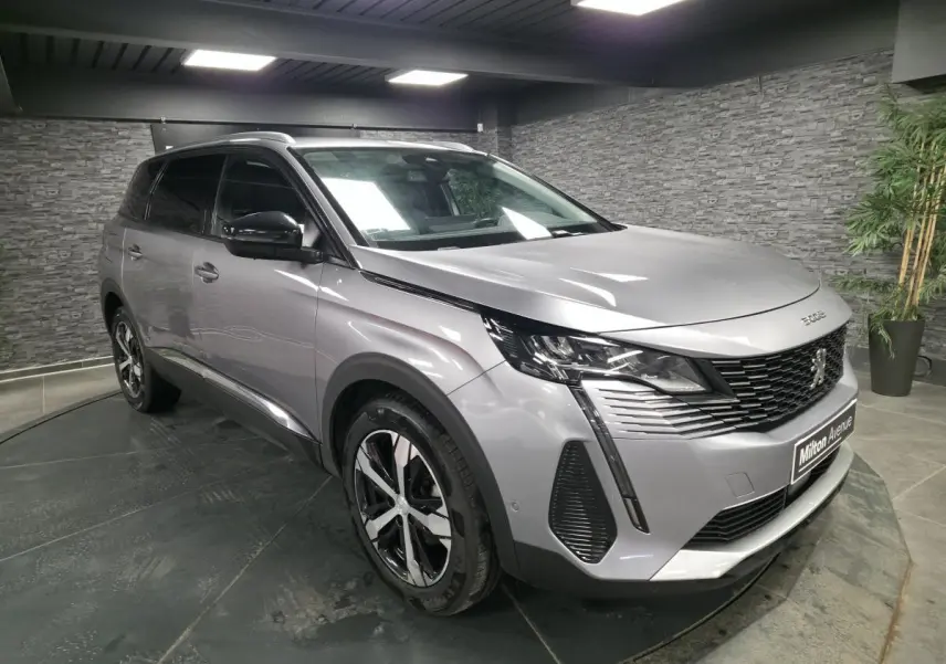 Peugeot 5008 gris métallisé vue 3/4 avant droit, avec calandre à damier chromé et jantes alliage bi-ton.
