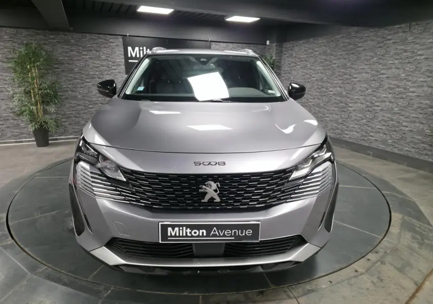 Vue frontale d'un Peugeot 5008 gris métallisé avec calandre à damier chromé et barres de toit visibles.
