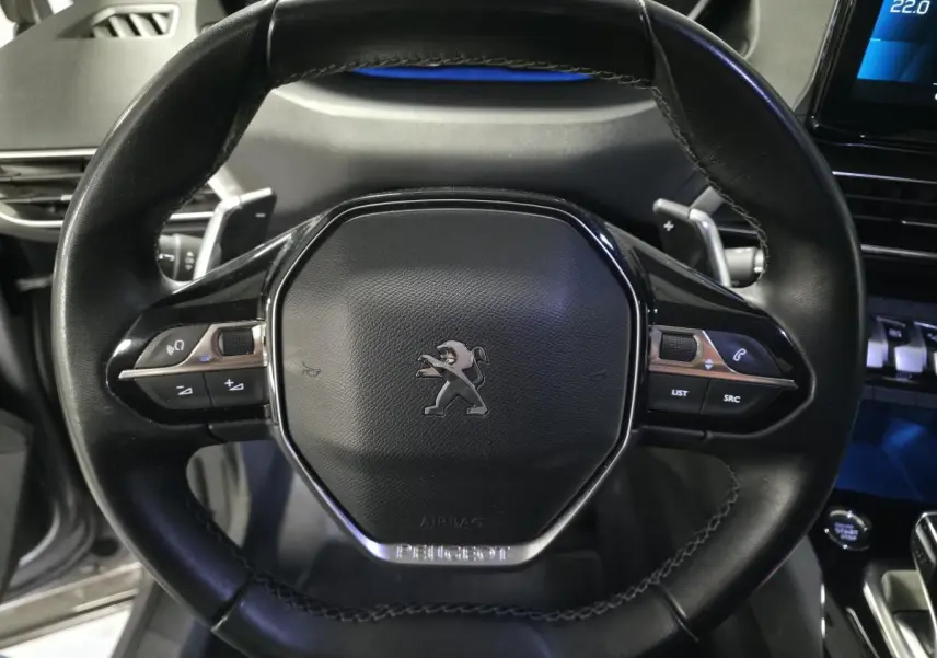 Gros plan sur le volant cuir noir du Peugeot 5008 2022 avec commandes intégrées et logo lion central.