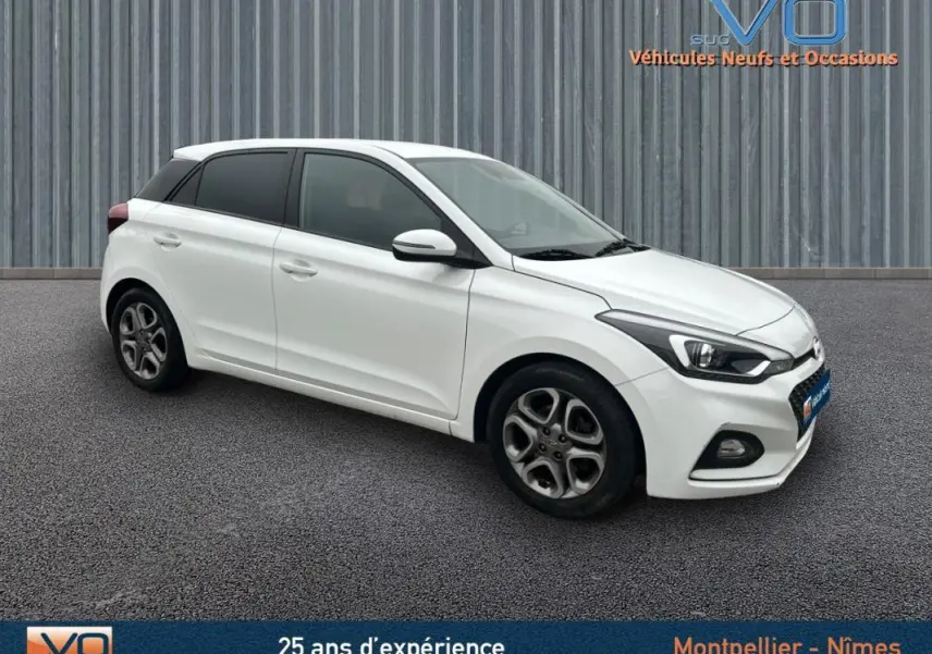 Hyundai i20 blanc vue 3/4 avant droit, jantes alliage 16 pouces et phares antibrouillard visibles