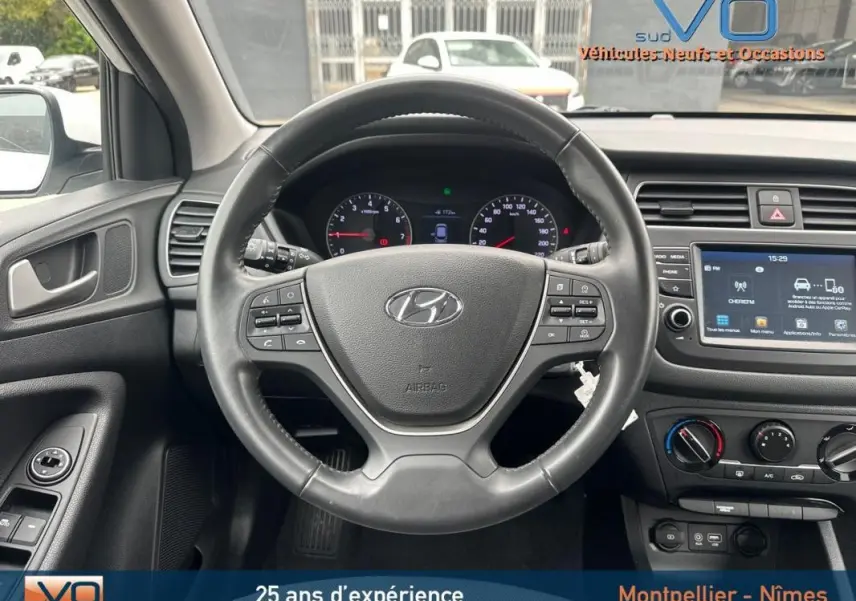 Vue intérieure centrée sur le volant noir de la Hyundai i20 blanche 2019 avec tableau de bord et écran tactile visible.