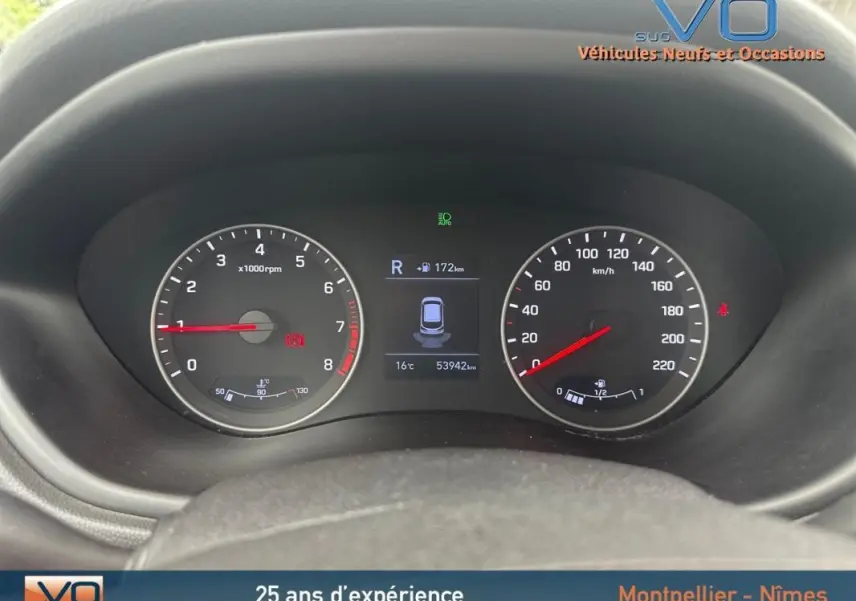 Gros plan sur le tableau de bord numérique de la Hyundai i20 blanche, affichant compte-tours et vitesse, avec écran central actif.