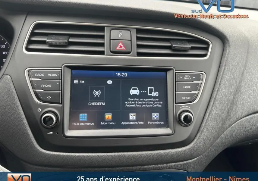 Vue rapprochée du tableau de bord de la Hyundai i20 blanche 2019, mettant en valeur l'écran tactile multimédia et les commandes environnantes.