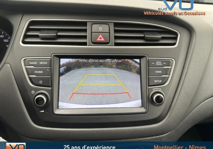 Écran central de la Hyundai i20 blanc 2019 montrant la caméra de recul avec guidage coloré, tableau de bord noir.