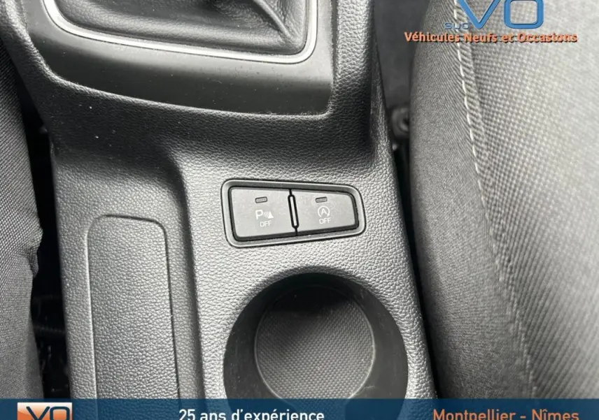 Gros plan sur la console centrale noire de la Hyundai i20 blanche 2019, montrant les boutons de désactivation du parking et du start-stop.