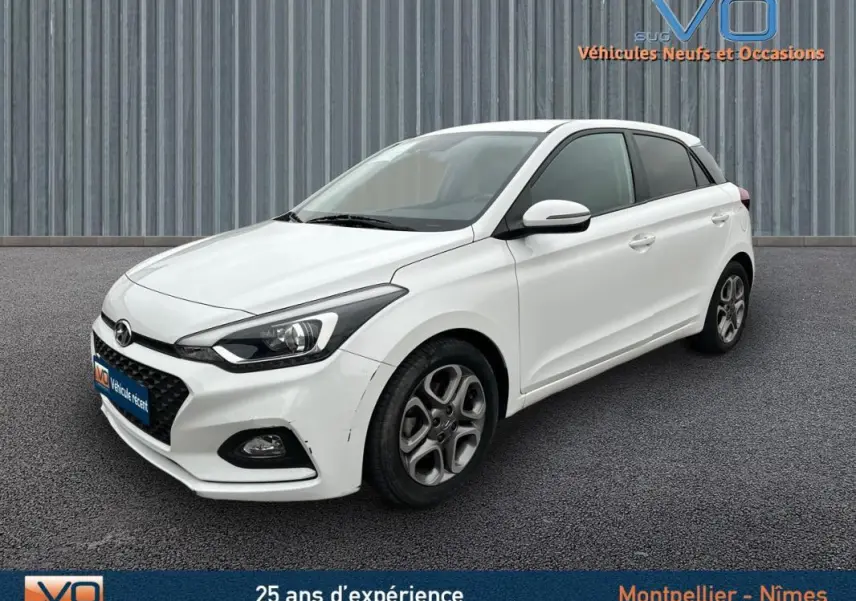 Vue 3/4 avant droite d'une Hyundai i20 blanche 2019 avec jantes alliage et phares LED distinctifs.
