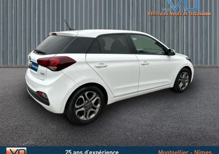 Vue 3/4 arrière droite d'une Hyundai i20 blanche de 2019 avec jantes alliage et vitres teintées arrière.