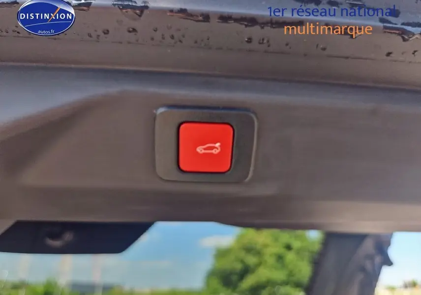 Bouton rouge d'ouverture électrique du coffre sur Peugeot 3008 noir, vue en gros plan depuis l'arrière du coffre ouvert.