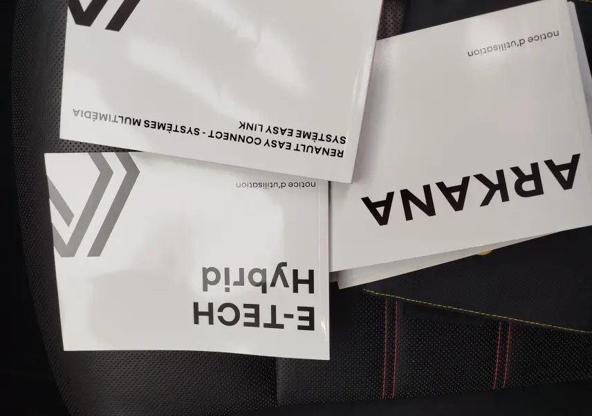 Manuels du Renault Arkana 1.6 E-Tech 145ch RS Line 2022 posés sur un siège noir avec surpiqûres rouges.