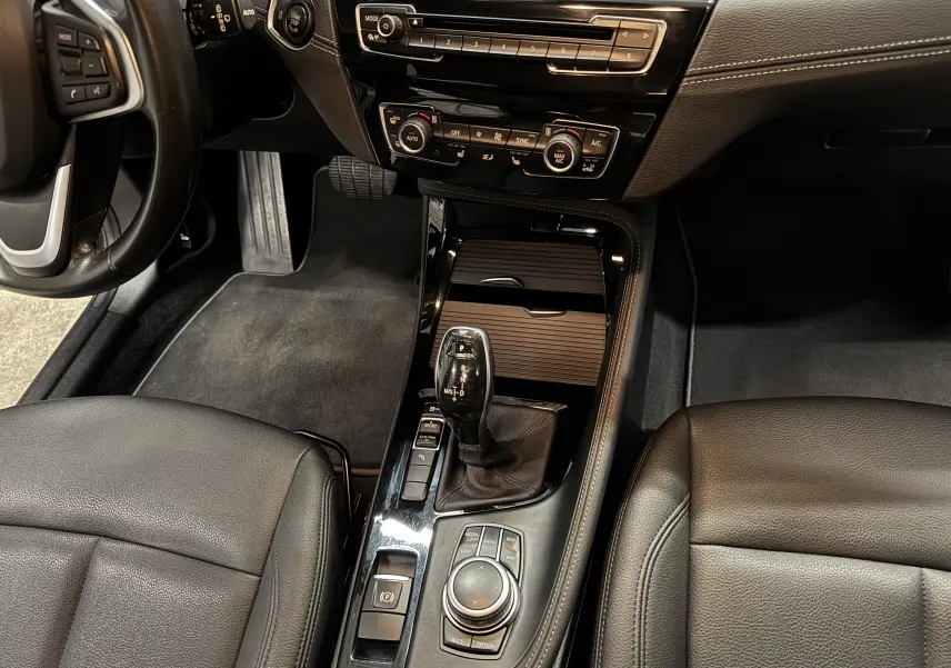 Vue intérieure centrée sur la console centrale et levier de vitesses d’une BMW X2 16dA Lounge Plus cuir noir.